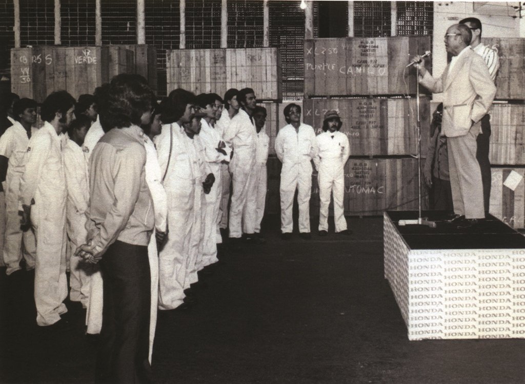 1974 – Soichiro Honda discursa para sua pequena equipe nas então tímidas instalações da Honda em São Paulo, onde hoje existe o imponente prédio administrativo da empresa atrás do Shopping Morumbi, em São Paulo. O primeiro, de jaqueta cinza, é Milton Benite, recém contratado da empresa. – Foto Acervo Murakami / Motostory